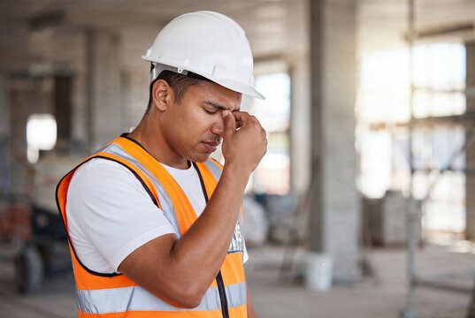 Exhausted construction worker wearing hard hat and reflective safety vest rubbing his eyes at an unfinished building site, showing fatigue, headache, stress and workplace strain with copy space.