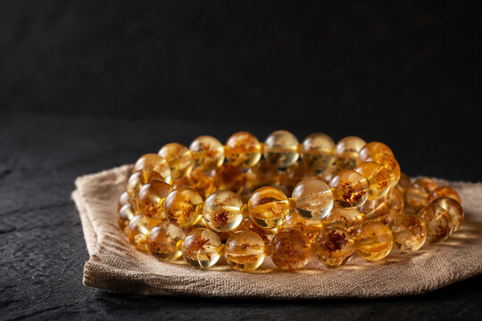 Honey-colored resin bead bracelet on linen cloth, organic plant inclusions, dark slate background, amber tones, jewelry presentation