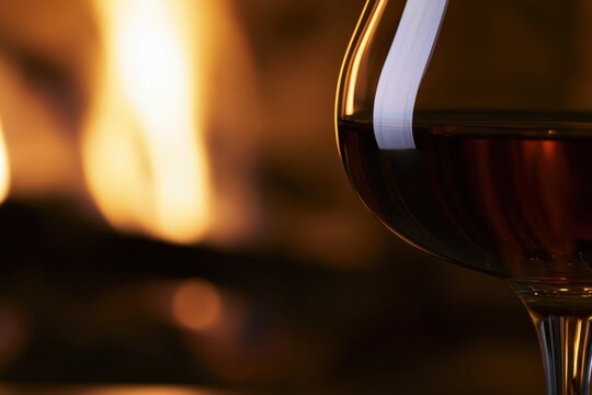 Close-up of dark amber whiskey in an elegant stemmed glass with warm fireplace glow and soft bokeh, creating a refined autumn hospitality atmosphere.