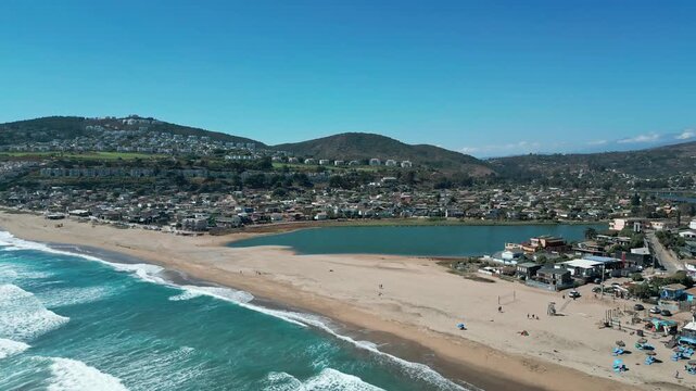 Aerial view of the coastal town of Maitencillo with its sandy beach, ocean waves, and hillside residential area in Maitencillo, Valparaiso, Chile.