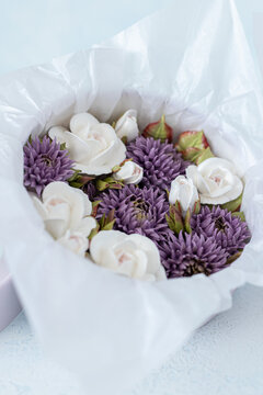 Floristry from Zephyr. White roses and purple flowers arranged in a gift box lined with tissue paper on a light blue background, perfect for special occasions