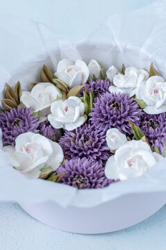 Floristry from Zephyr. White and purple artificial flowers arranged in a round white box with tissue paper, showcasing a decorative floral design for home decor or gifting