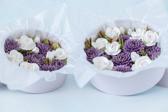 Floristry from Zephyr. Floral arrangement featuring white roses and purple asters in round boxes lined with tissue paper on a light blue background