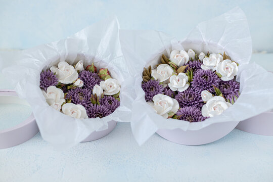 Floristry from Zephyr. Floral arrangement in round purple boxes featuring white roses and purple asters, elegantly presented with tissue paper on a light background