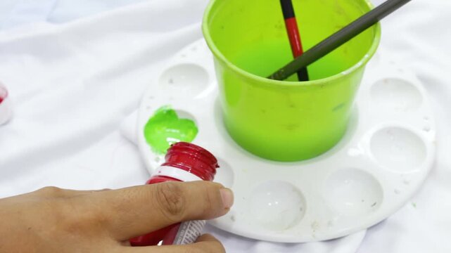 The hands of an unrecognizable woman are preparing a color palette with red tempera paint on a table inside a sewing workshop in Neiva, Huila, Colombia. Concept of handmade and hobbies