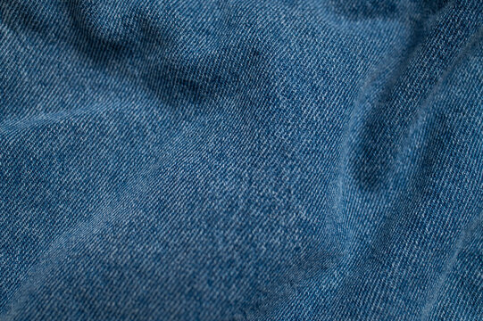 Blue denim fabric with soft waves fills frame in close-up. Denim texture and folded textile surface create versatile visual background for fashion, apparel, branding and design projects.