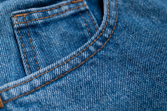 Blue jeans pocket detail shows orange stitching, denim weave, and curved seam in close-up. Cotton textile texture suits apparel marketing, fashion education, product catalogs, and design.