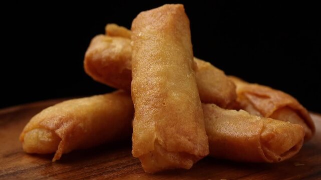 Crispy fried spring rolls on a wooden plate rotating on a black background.