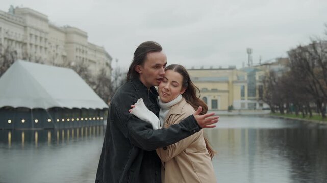 Close up of man and woman standing by calm water body in urban park sharing intimate moments. couple interacts closely with soft lighting reflecting on lake behind them surrounded by bare