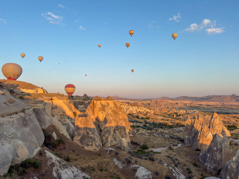 Hot air balloons fly over Goreme valleys at sunrise in Cappadocia, Turkey.