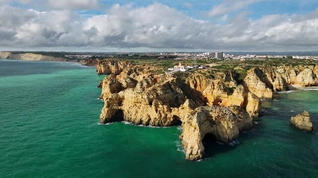 Aerial view of Ponte da Piedade in Lagos, Algarve, Portugal, with ocean cove, sea stacks and rugged cliffs. Push in tilt down shot.