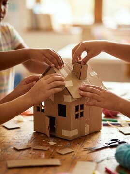 Children crafting a miniature cardboard house model on a wooden table. Joyful teamwork and creative play during an art class. World Children's Day World Childrens Day celebration of.