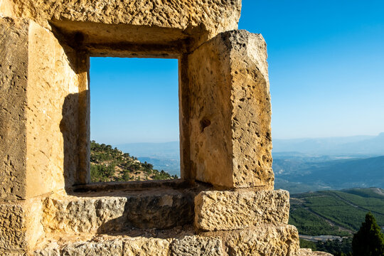 Ancient stone of Alahan monastery window offers panoramic view of rolling hills and sky