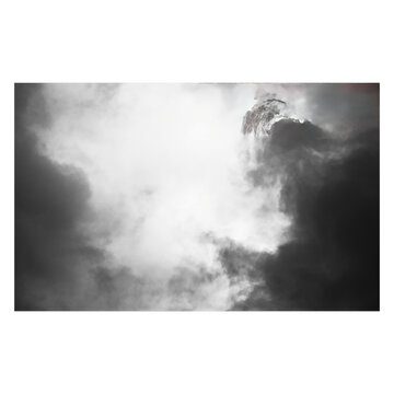 A grayscale photograph of thick, billowing smoke or clouds filling the frame, with a bright, overexposed white light source in the center.