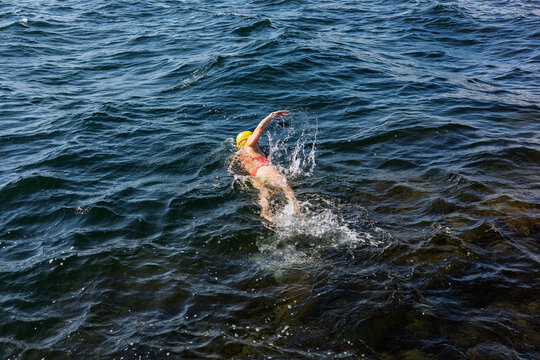 A woman swimming freestyle in the wavy deep blue sea of the Baltic coast on a sunny day, embodying energy, health, and freedom