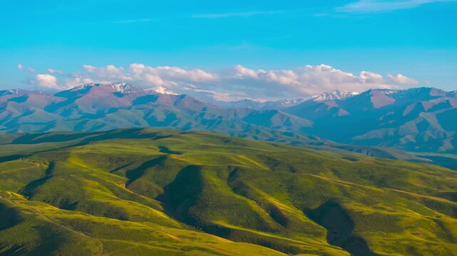 drone hyperlapse above rolling green hills and snowcapped mountains at the horizon in summer Kyrgyzstan