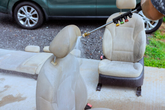 Service worker uses pressure washer to clean car seats outside on driveway.
