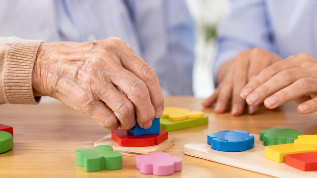 Senior woman hands solving wooden puzzle with caregiver. Cognitive therapy activities for brain health, dementia and alzheimer care. Support and rehabilitation in aging concept.