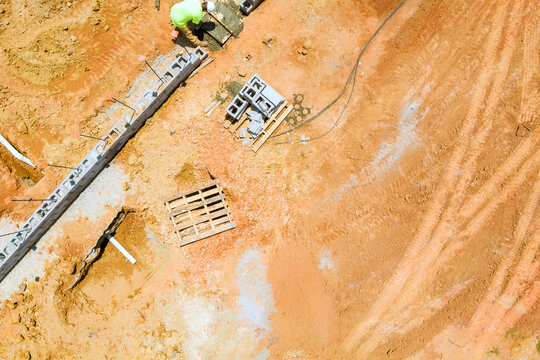 Workers are building foundation structure using various materials at site area is covered in dirt, machinery.