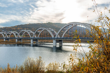 Long railway arch bridge crosses water near Zembrzyce and Jezioro Mucharskie, framed by autumn hills and reflective reservoir water. Repeating concrete arches and vertical hangers create a strong imag © Volha