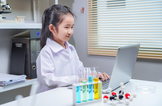 Asian girl in lab coat typing on laptop with test tubes for science education and stem learning