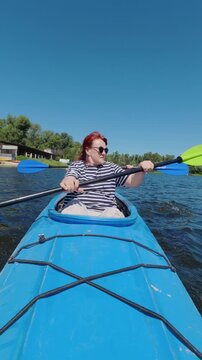 Woman paddling a blue kayak on a sunny river during summer vacation