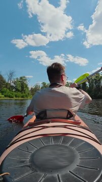 Rear view of man paddling tandem kayak on calm river for outdoor adventure concept