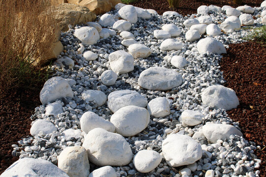 Galets d&eacute;coratifs en marbre blanc dans un am&eacute;nagement paysager ext&eacute;rieur avec gravillons gris et paillage rouge