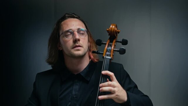 Caucasian young adult man playing cello, camera zooming in and tilting up as he performing music. Ideal for classical music promotions, artistic documentaries, or concert advertisements