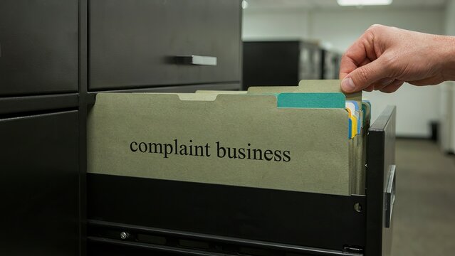 Complaint business folder being pulled from a metal filing cabinet drawer in an office setting.