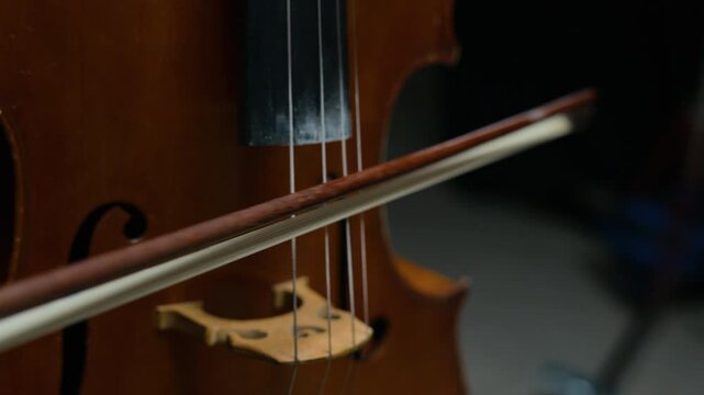 Caucasian man playing cello, drawing bow across strings in closeup shot. Clip is perfect for classical music education promos or orchestral performance advertisements
