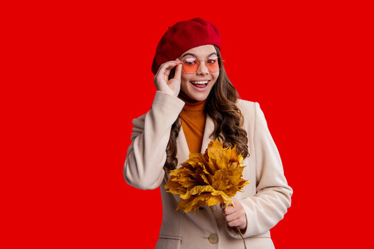 Fall season beauty. Autumn style. Fallen autumn leaves. September season. Stylish teen girl isolated on red with maple leaf. Autumn leaf arrangement. Girl with maple leaf wear hat. Autumn outfit