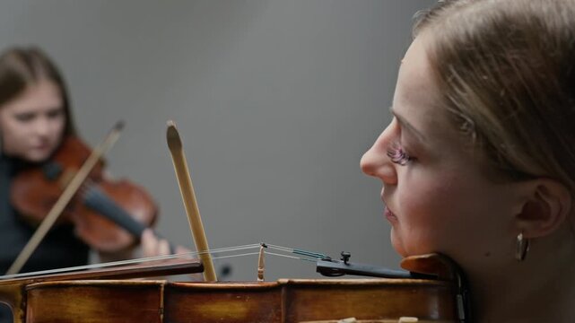 Caucasian young adult female violinists playing classical music during rehearsal, shifting focus from foreground to background player. For classical concert promotions or music education videos