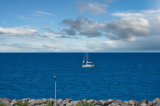 Sailboat on Deep Blue Sea Near a Breakwater Under Cloudy Sky