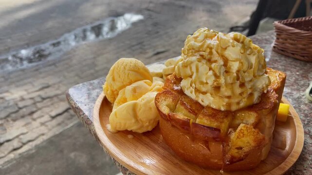 Close-up of toasted bread topped with vanilla ice cream, banana slices and whipped cream while honey is drizzled over the dessert at a caf&eacute;