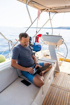 Focused man working on laptop aboard a sailing yacht. Productive remote office in a unique travel environment.
