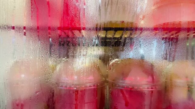 close-up motion of multiple pink and red frozen food like watermelon seen through condensation covered refrigerator glass, showing vertical bead accumulation and rivulets glass