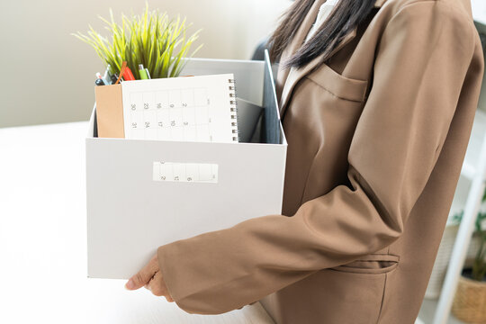 Unemployed, quite job. Desperate asian young businesswoman resigning from company, hand holding cardboard, packing belongings, stuff into box, layoff or changing work. Resignation, employment concept.