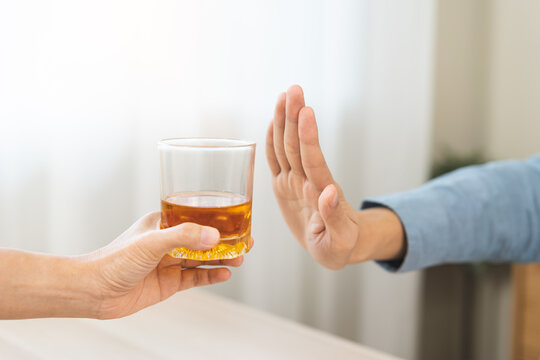 Close up of Asian young man making stop hand gesture to refuse a glass of whiskey, responsible man saying no to alcohol drink, stop alcoholism and addiction social problem, health care concept