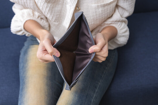 Woman showing an empty wallet with no money at home, representing financial hardship, cash shortage, personal debt, budget problems, rising expenses, poverty, cost of living crisis.