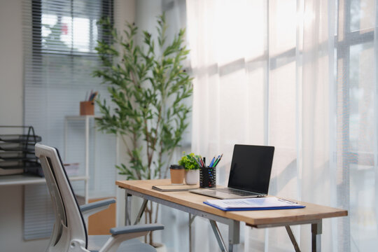 Minimalist home office setup with an open laptop, coffee cup and organized supplies on a light wooden desk, bathed in soft natural daylight for focused remote work