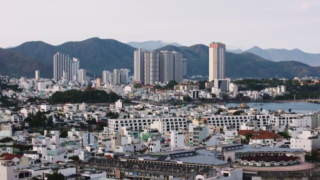 Panoramic view of nha trang's urban landscape. Showing a dense collection of buildings and modern skyscrapers with rolling green mountains creating a striking contrast against the city's architecturec
