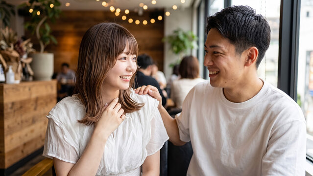 Young Japanese couple smiling and interacting affectionately in a modern caf&eacute;, romantic date scene
