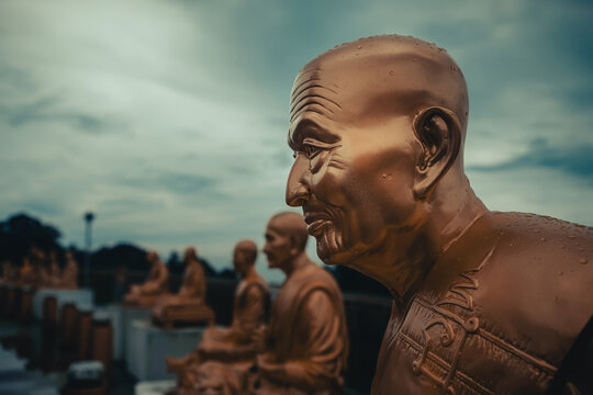 Close-up profile of a sacred golden monk sculpture with raindrops against a moody sky