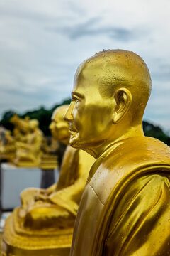 Close-up profile of a sacred golden monk sculpture with raindrops against a moody sky