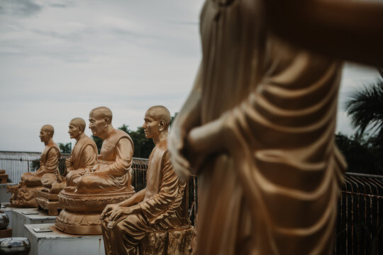 Close-up profile of a sacred golden monk sculpture with raindrops against a moody sky