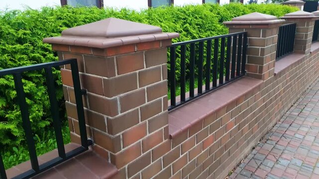 A brown brick fence. A brick fence around a house. A brick fence an architectural design element.