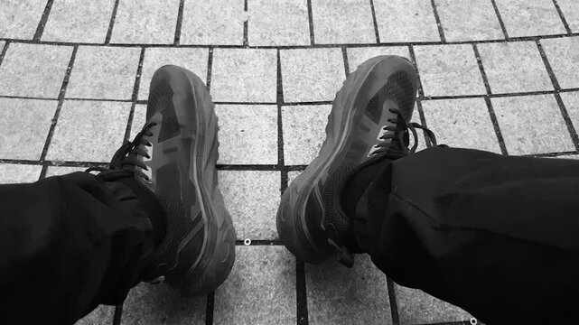 A man's legs POV in athletic shoes and pants. The man is crouching on a bench POV black and white