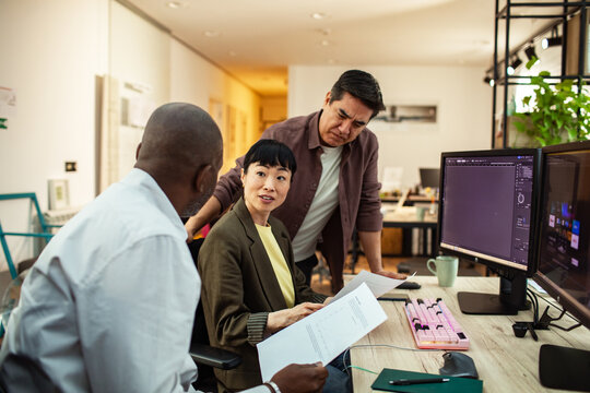 Coworkers discussing project at computers in modern office