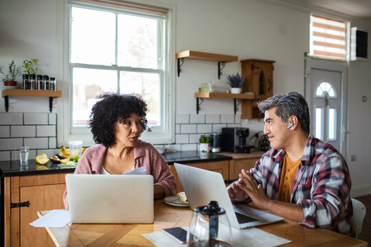 Mature couple discussing finances at kitchen table while working from home
